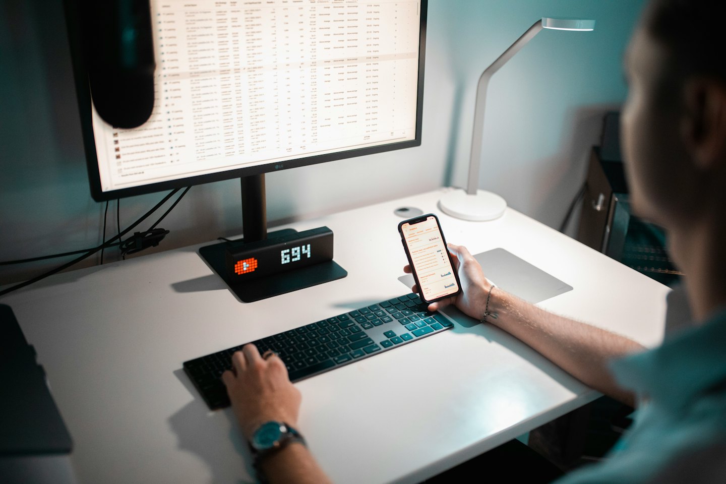 Person tippt auf einer Tastatur am Schreibtisch mit Computer und Telefon.